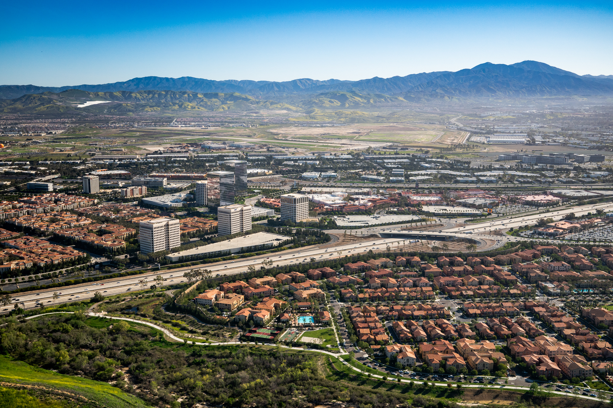 Aerial photography of a region in Southern California with a view of residential and commercial areas. Rolling hills can be seen in the background.