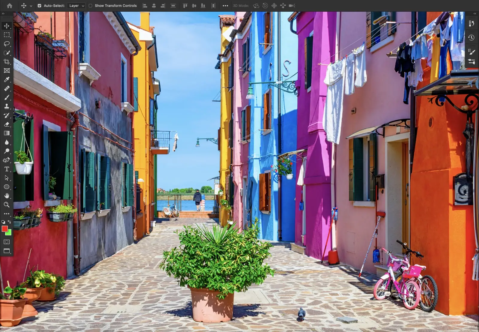Foto de bairro com casas coloridas, ao fundo está o mar, em primeiro plano uma planta e ao redor tem mais canteiros, roupas e uma bicicleta