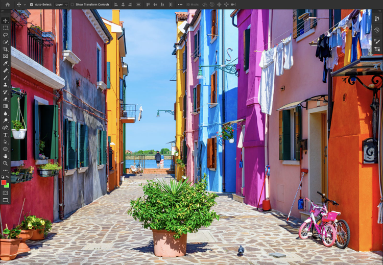 Foto de bairro com casas coloridas, ao fundo está o mar, em primeiro plano uma planta e ao redor tem mais canteiros, roupas e uma bicicleta