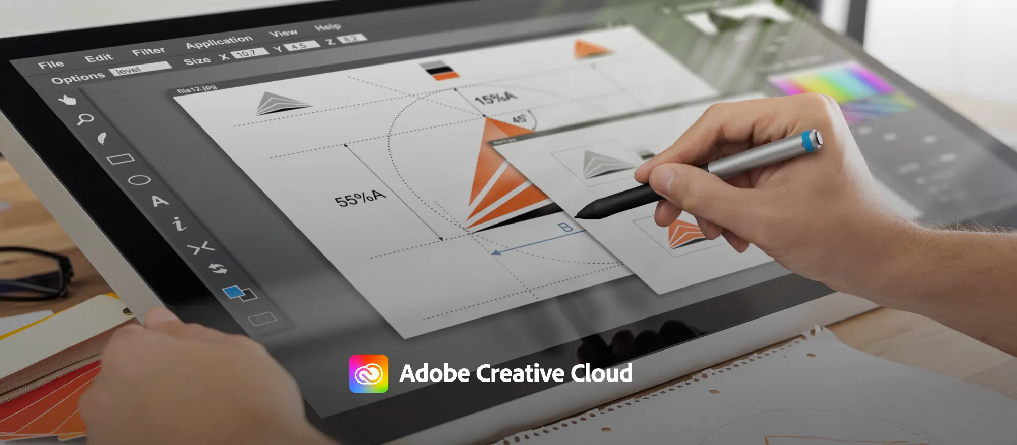 notebook com aplicativo de design aberto ao lado de uma mão segurando uma caneta eletrônica criando um logotipo