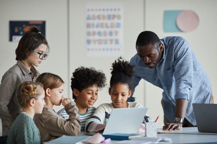 A group of children and a teacher looking at a laptop screen. 