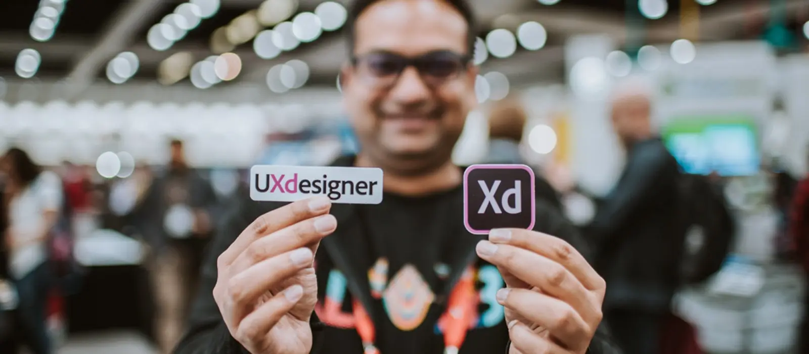 An attendee at Adobe MAX 2018 poses for the camera while holding UXdesigner and Adobe XD stickers.
