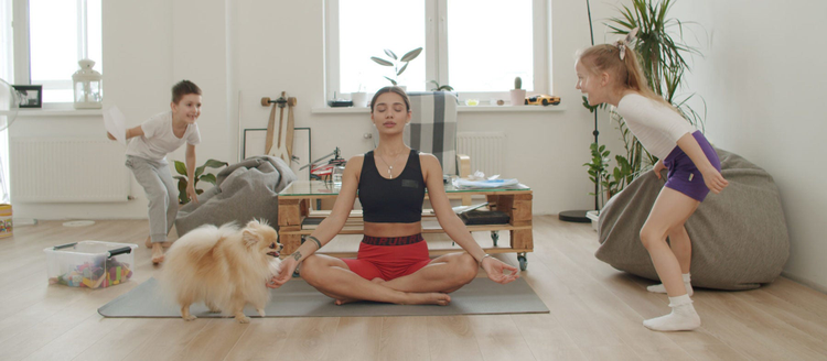 Mother meditating while kids and dog are playing