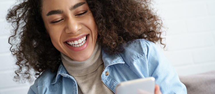 Cheerful afro american millennial woman holds smart phone watching social media stories video. Happy young mixed race teen girl mobile phone.
