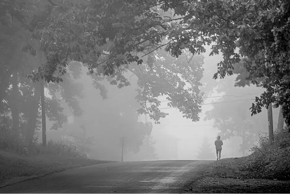 Black and white image of a person walking down a road.