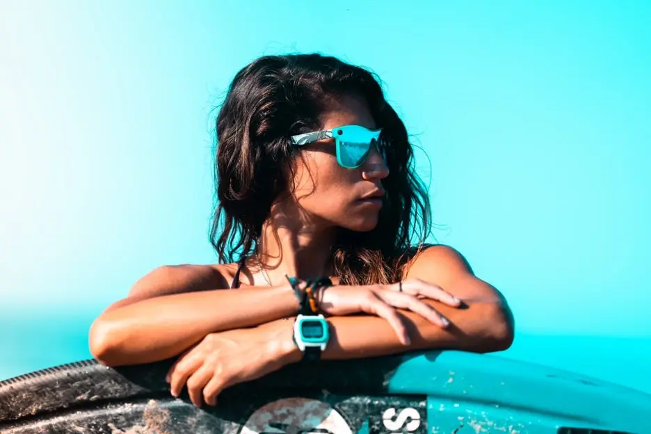 Woman with sunglasses on gazing at turquoise background.
