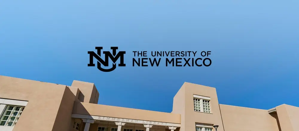 The University of New Mexico Logo against a blue sky and top of building. 