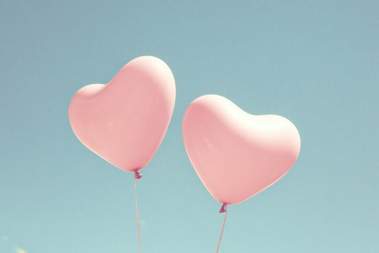 Two pink heart shaped balloons in turquoise sky