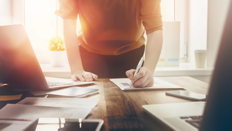 Woman writes on paper on desk.