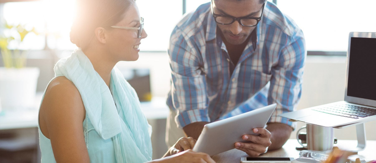 A man and a woman look at a tablet in an office.