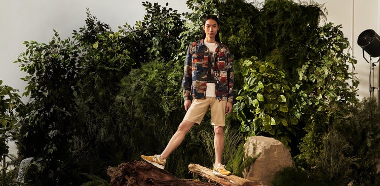 Man standing on logs in front of greenery.