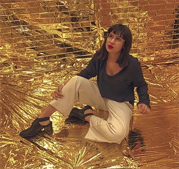Graphic designer, Khyati Trehan seated in a pose against a backdrop of gold foil.