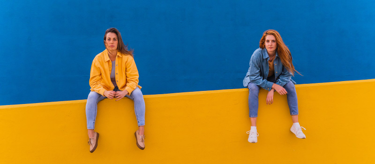 Young women sitting on an orange wall.