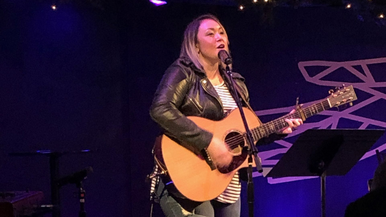 Denise playing her guitar and singing on stage.