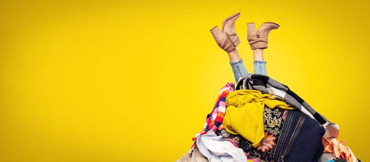 woman legs out of clothes pile on yellow background with copy space