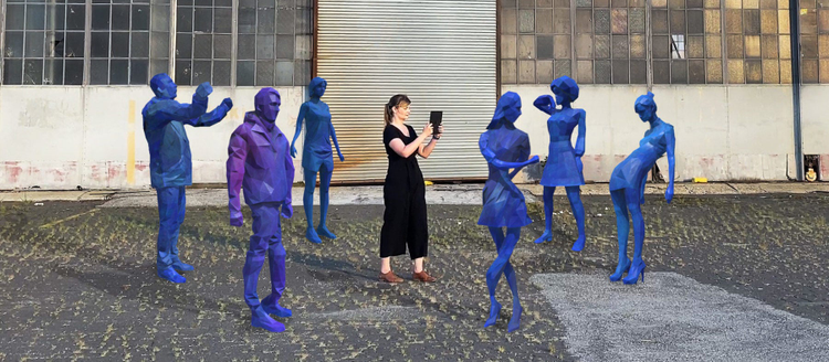 A photograph of a woman interacting with Gabriel Barcia-Colombo's Choir AR installation. The AR characters are superimposed on the image reflecting what the user sees on their phone.