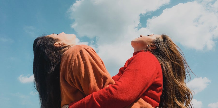 Two girls with arms around each other look up at the sky.