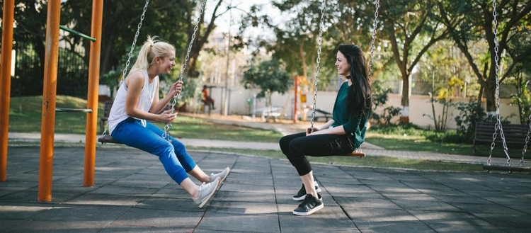 2 girls talking while on swings.