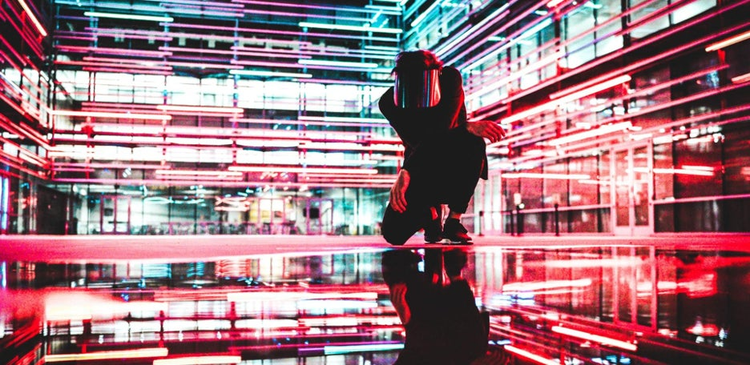 Man kneeling with neon lights behind.