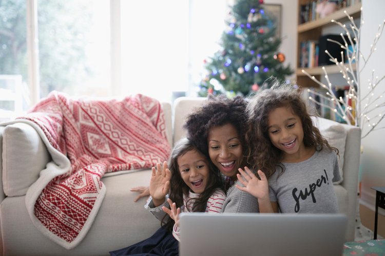 Mother and two daughters waving at computer screen with Xmas tree in background