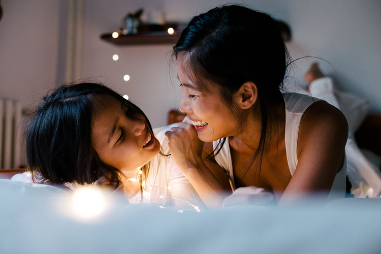 Photo of young woman and child in bed laughing