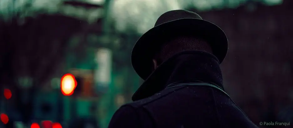 Man in dark city with coat and hat on.