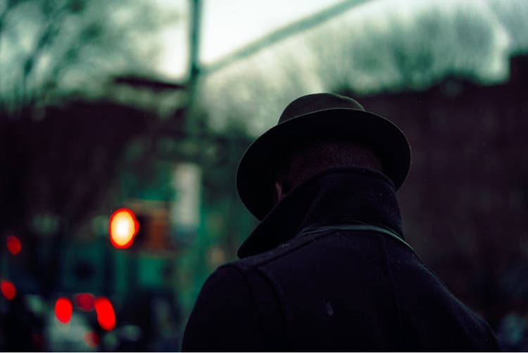 Man in dark city with coat and hat on.