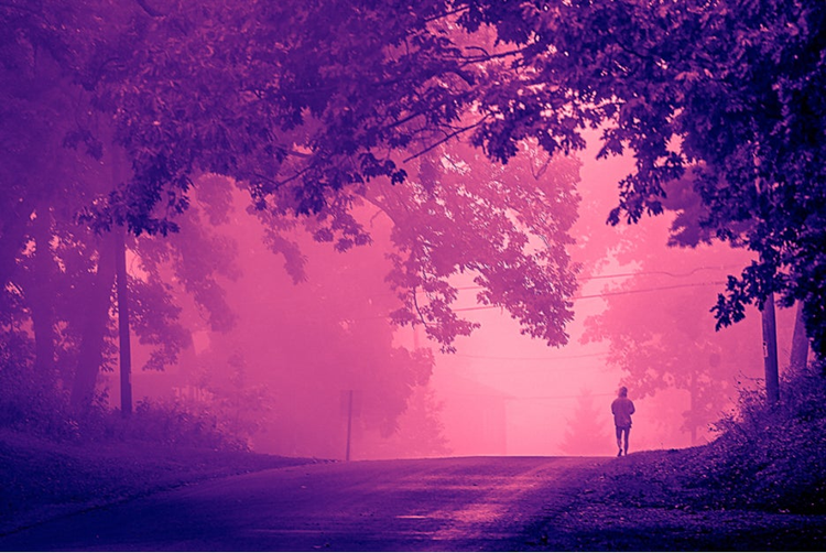 Red and blue color graded image of a person walking down a road.