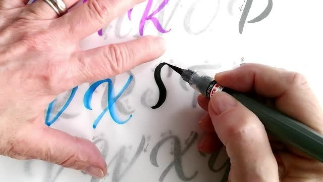 Hands of someone brush lettering.
