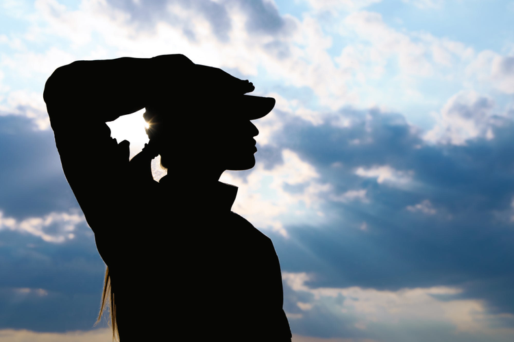 Female soldier in uniform saluting outdoors.