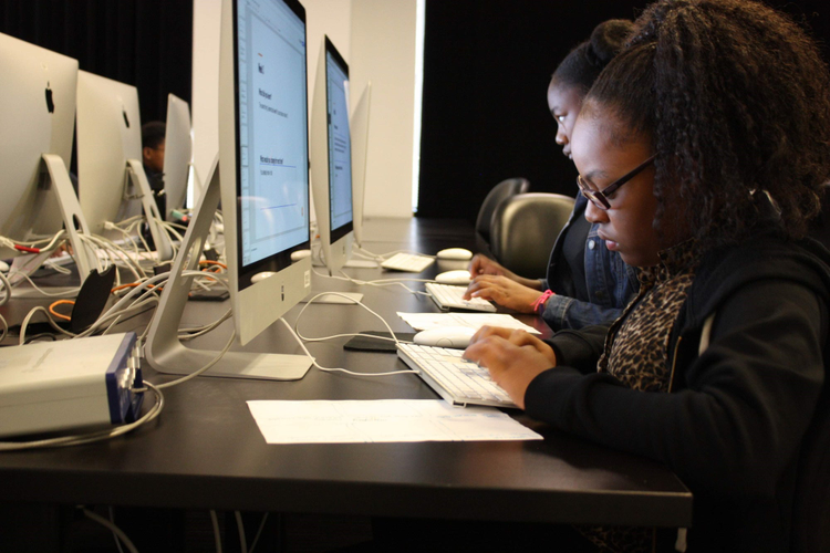 Two students typing on keyboards in front of computer screens. 