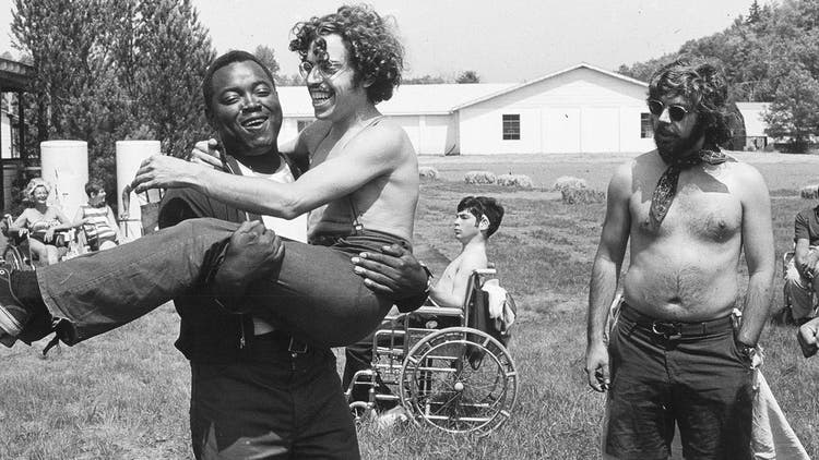 Man being carried by another man, still image from Crip Camp documentary.