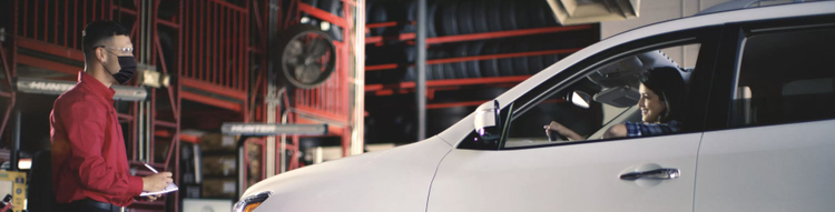 An add showing a Discount Tire employee in a mask talking to a customer sitting in her car.