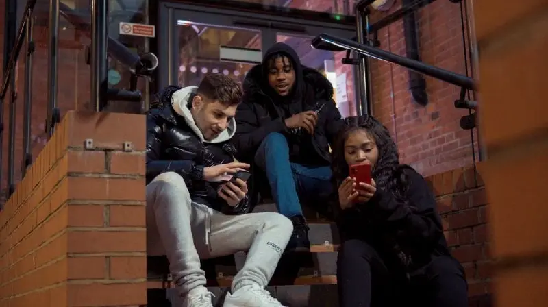 Three people sitting on stairs looking at devices. 