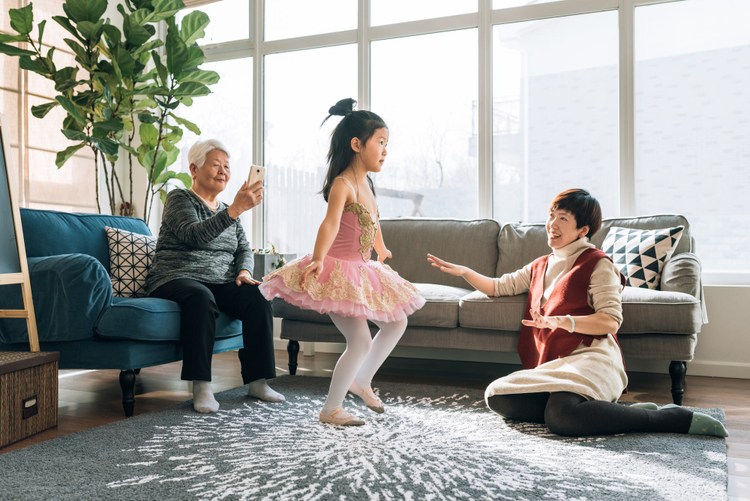 Little girls dressed in baller costume dancing while two woman watch and take a picture of her. 