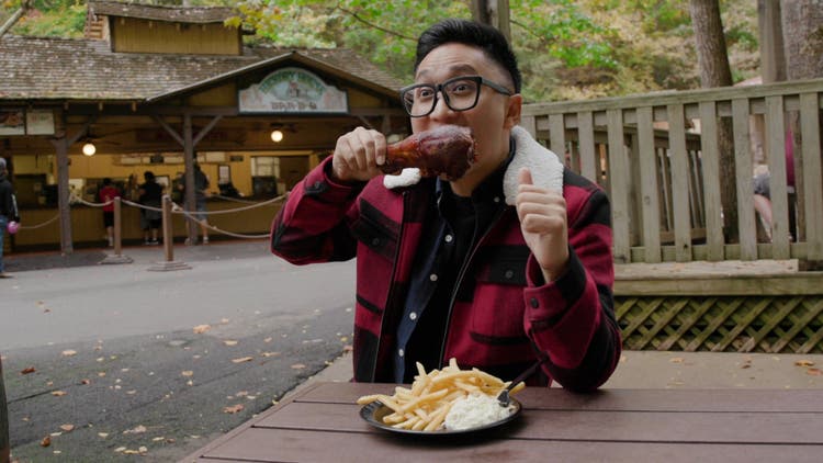 Man Eating a turkey leg at a picnic table outfoors.