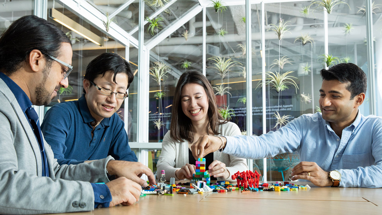 Group of 4 people at a table building with legos. 