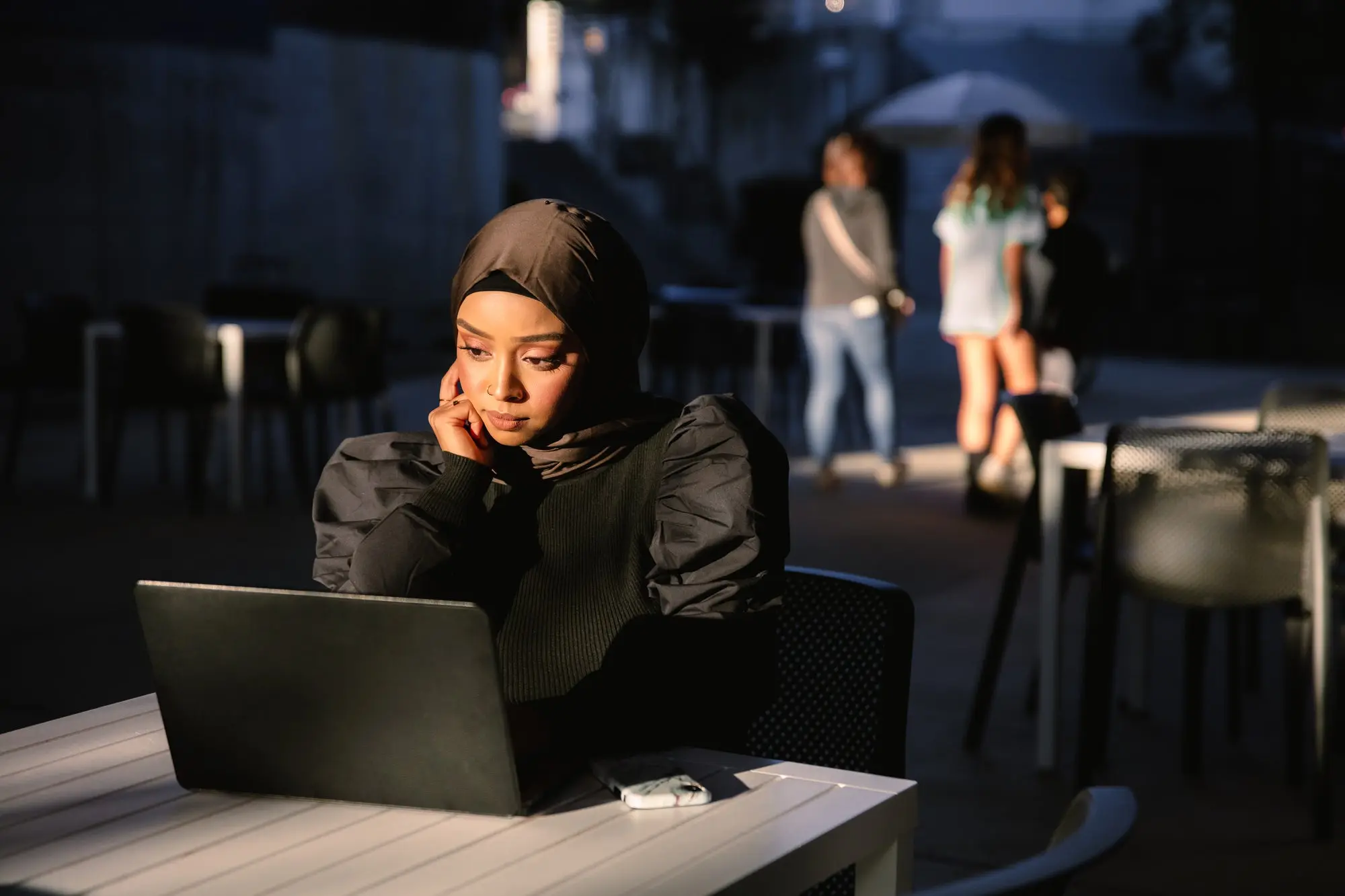 Woman sitting at a table outside looking at a laptop. 