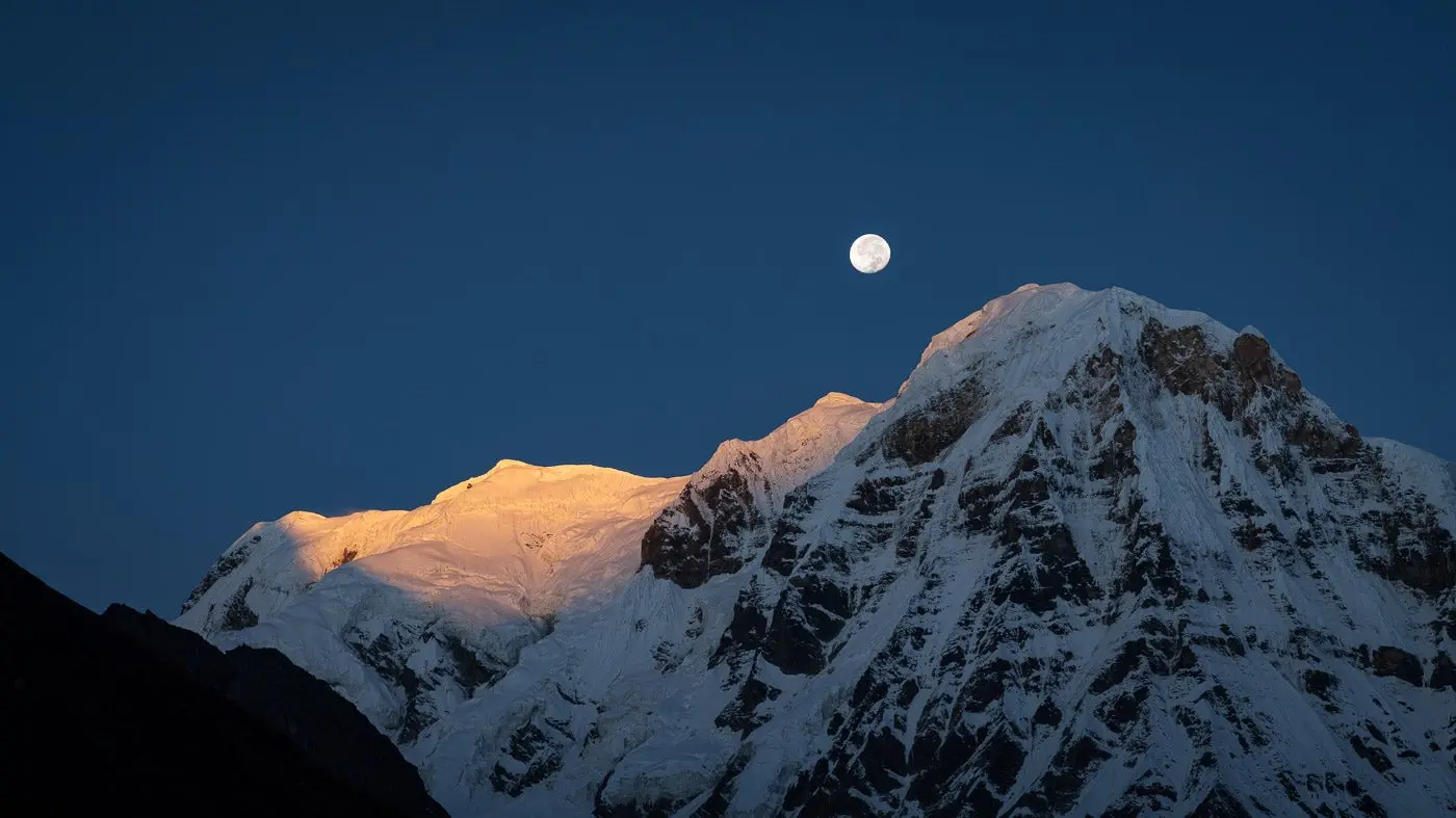 Photo of a snowy mountain with light from the moon shining on top.
