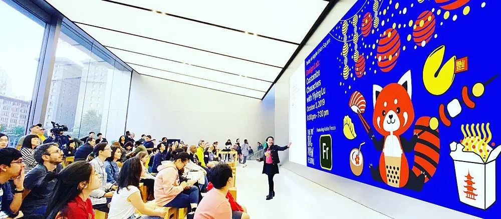 Yiying Lu stands on stage in front of a big crowd, with her emoji designs for the Hungry Red Panda book in the background.