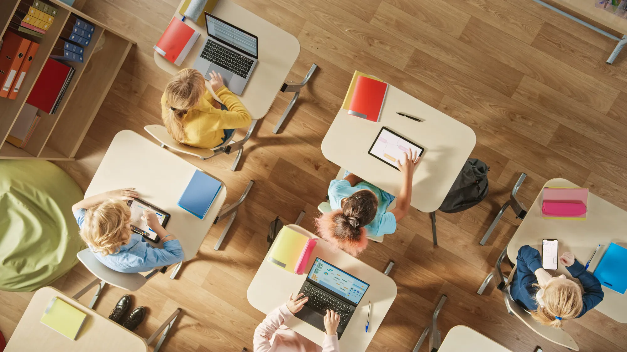 Top view shop of kids at desks on electronic devices.