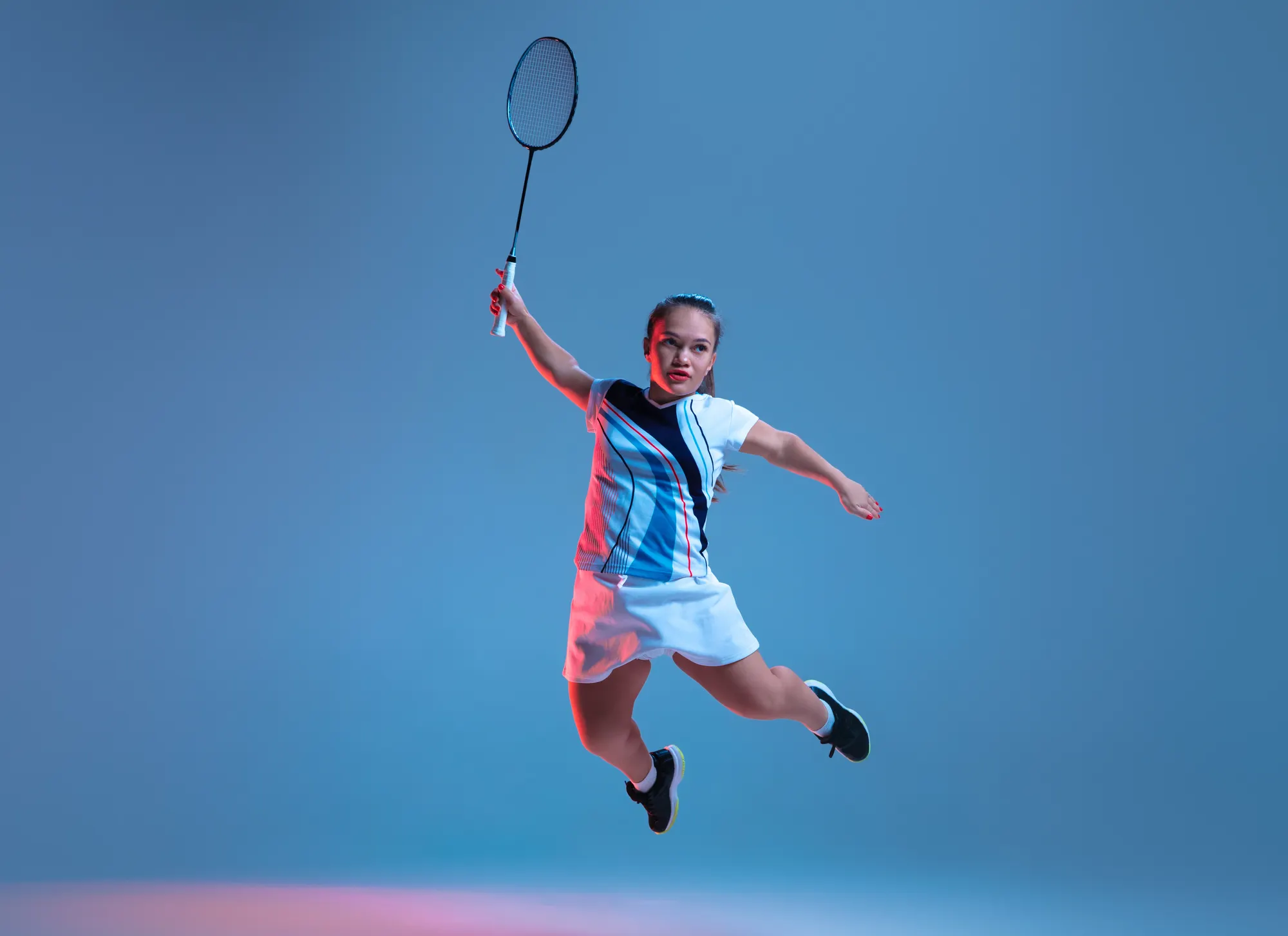 Girl jumping with a tennis racket. Behind her is a blue background.