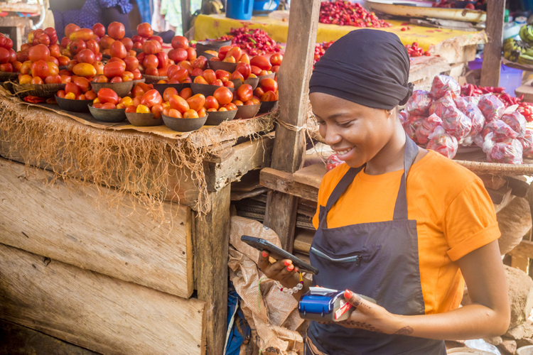 Woman at a vegtable stand looking at her phone. 