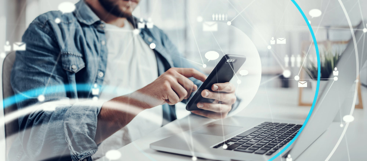 Man on his phone while in front of his laptop. 