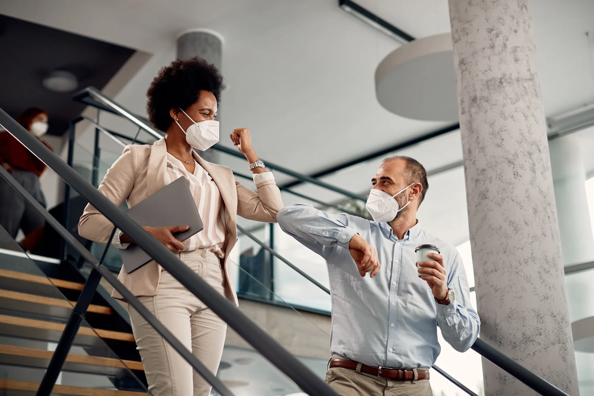 Woman and man wearing masks, interacting through an elbow bump.