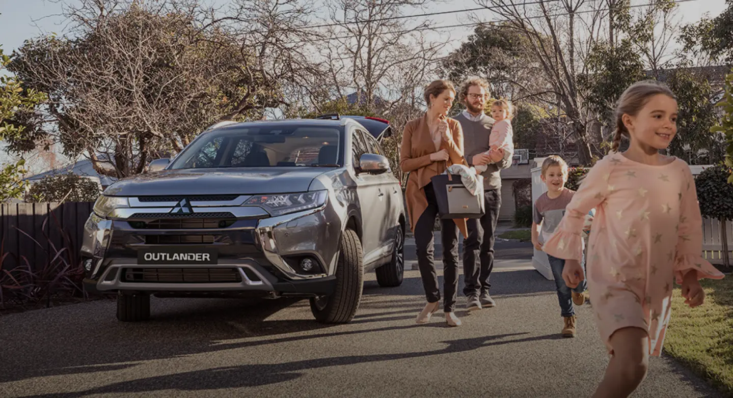 Familyl walking next to a Mitsubishi Outlander car.