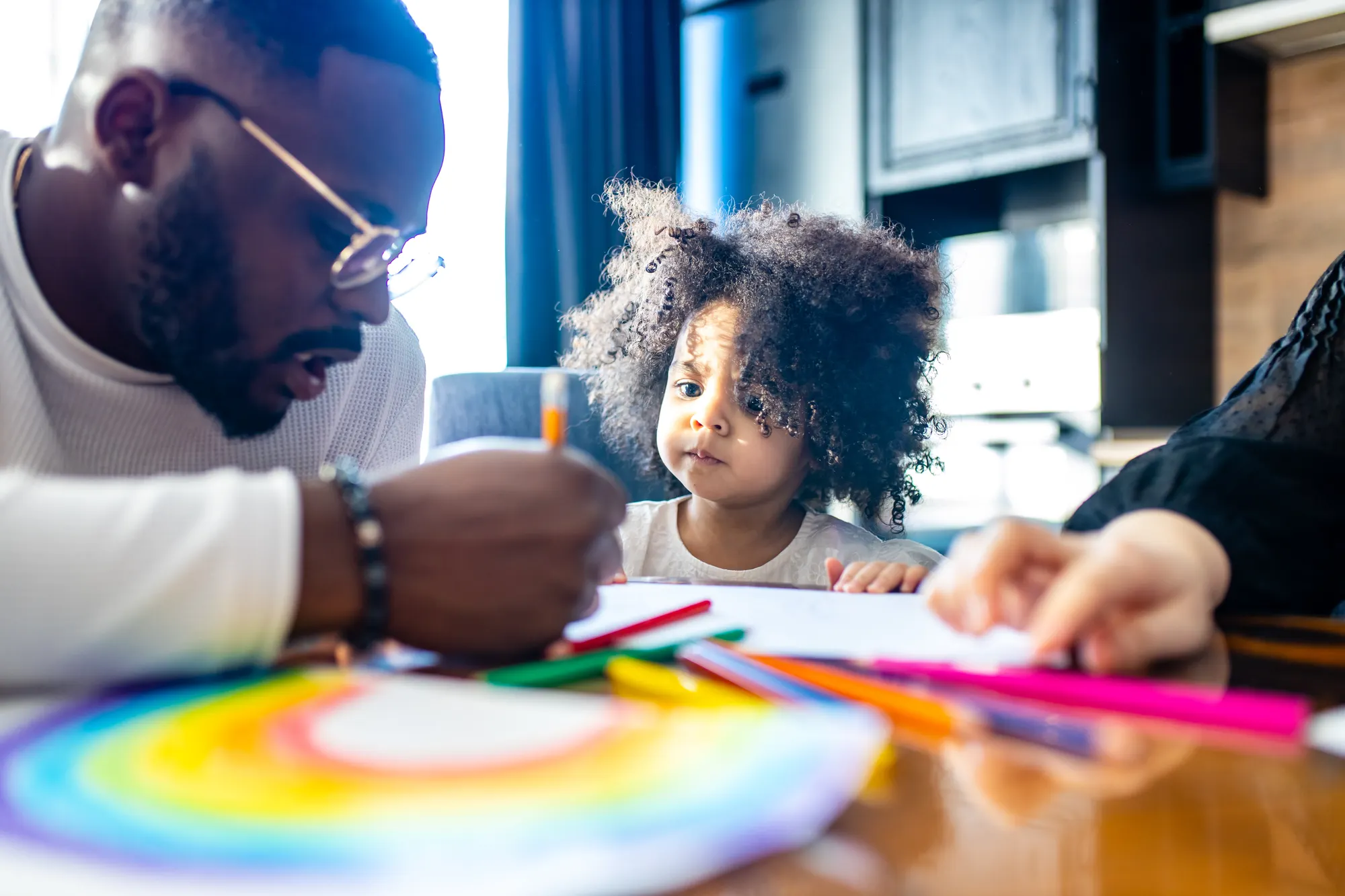 Young girl drawing rainbow with family