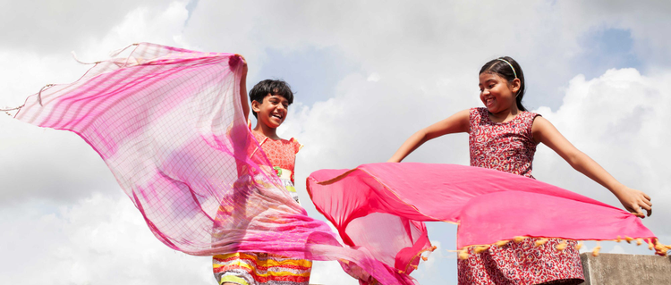 Two young girls holding pink scarfs and dancing. 