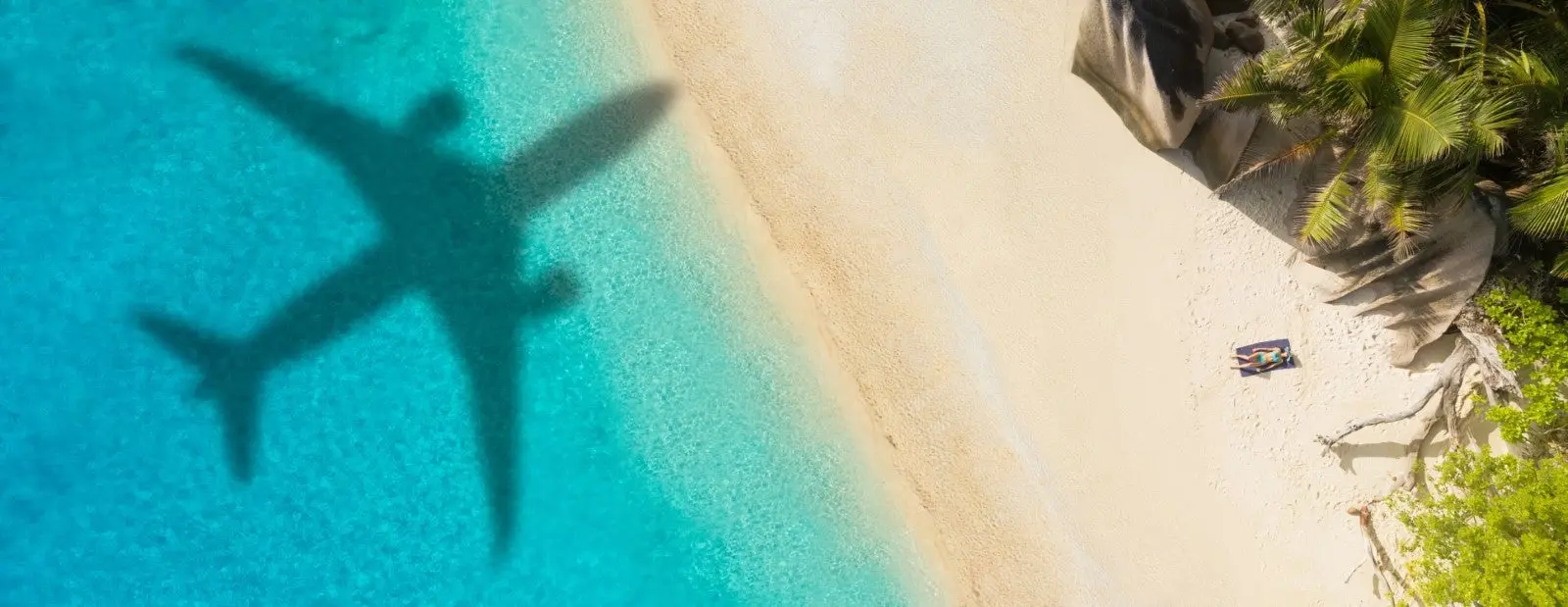 Shadow of a plane flying overhead on a beach with turquoise water. 