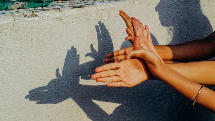 Photo of someones hands making shadows on the ground. 
